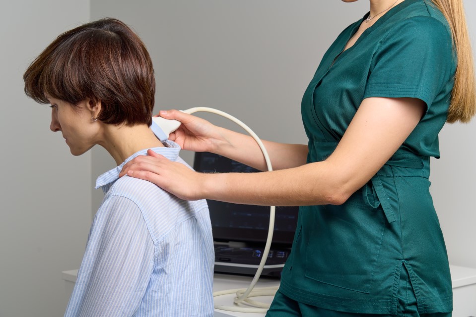 Kobieta bada pacjenta za pomocą aparatu USG na szyi, co ilustruje profesjonalną diagnostykę i leczenie fizjoterapeutyczne wdowiego garbu.